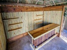 Wooden tiki bar with bamboo paneling and shelves. Palm thatch roof.