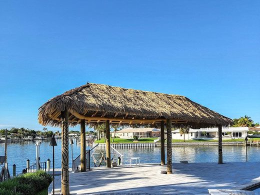 Tiki hut on a dock overlooking water; blue sky, sunny day; residential area in the background.
