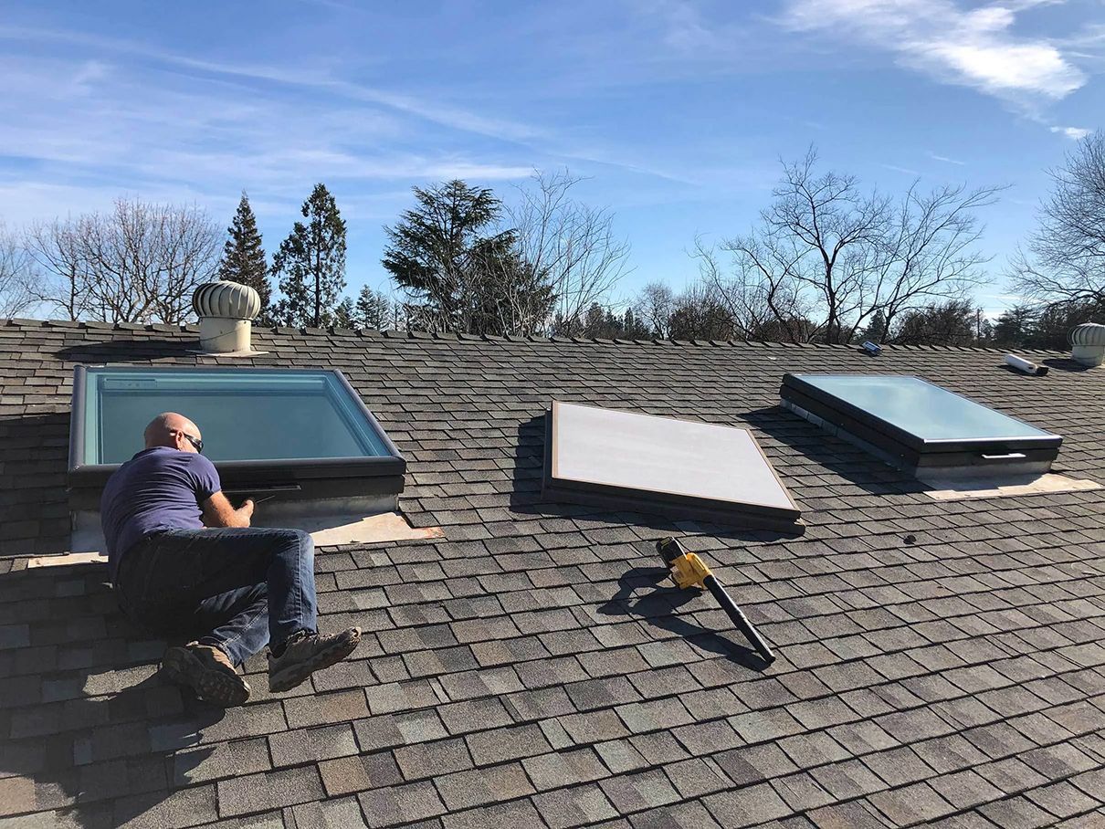 A man is sitting on top of a roof with skylights.