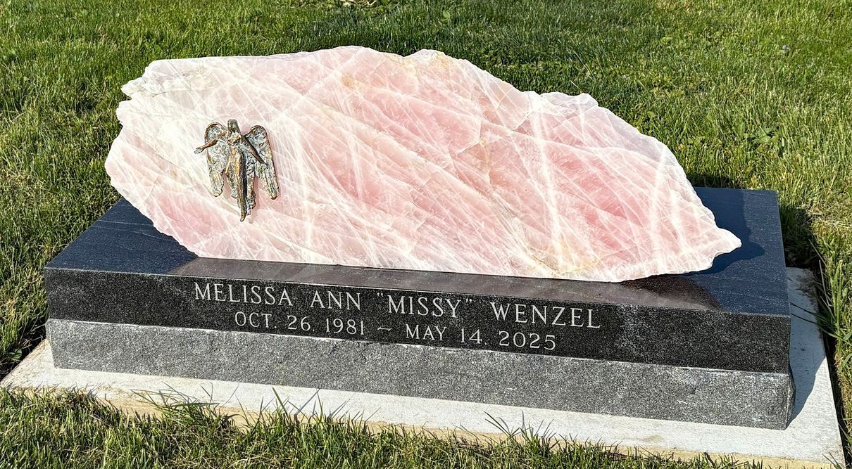 Pink rose quartz memorial on a black granite grave marker in a grassy cemetery