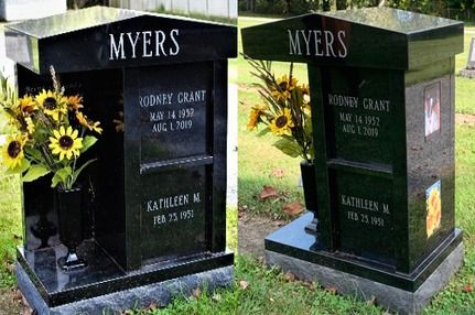Two black memorial headstones with yellow flowers beside one grave in a grassy cemetery