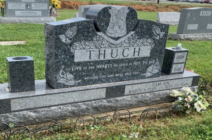 Granite gravestone with “THUCH” engraved, surrounded by flowers in a cemetery