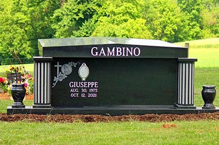 Black cemetery headstone engraved “GAMBINO” with flowers, set on green grass