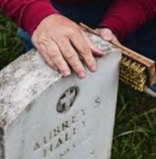 A hand brushes dirt off a white gravestone in grass.