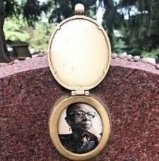 Oval memorial locket with a black-and-white portrait set into a pink granite headstone outdoors