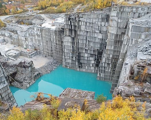 Bright turquoise quarry lake surrounded by gray stone walls and yellow autumn trees