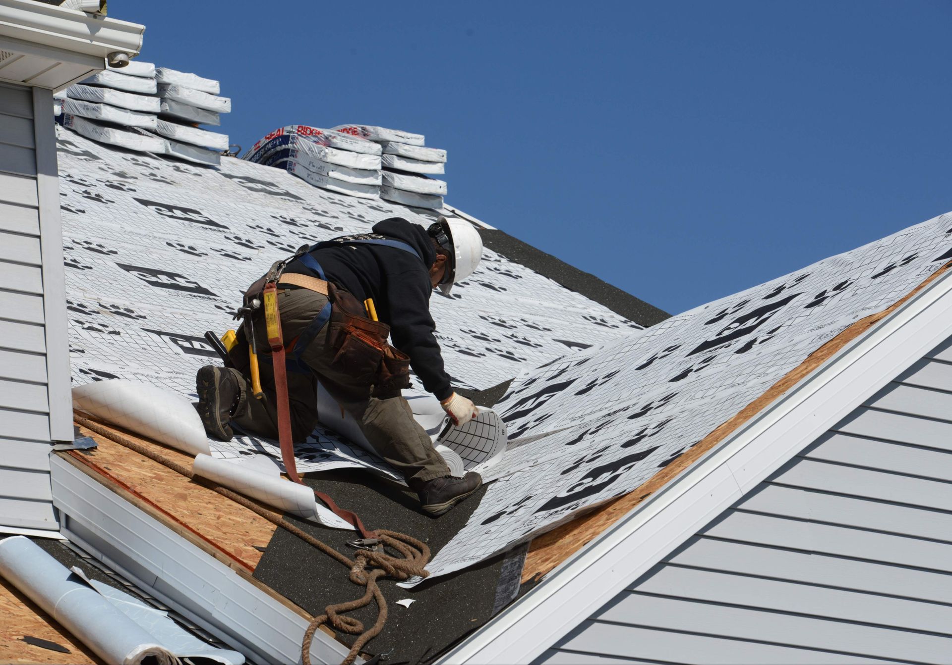 A man performs roof maintenance, replacing broken shingles with new ones on an uncovered roof.