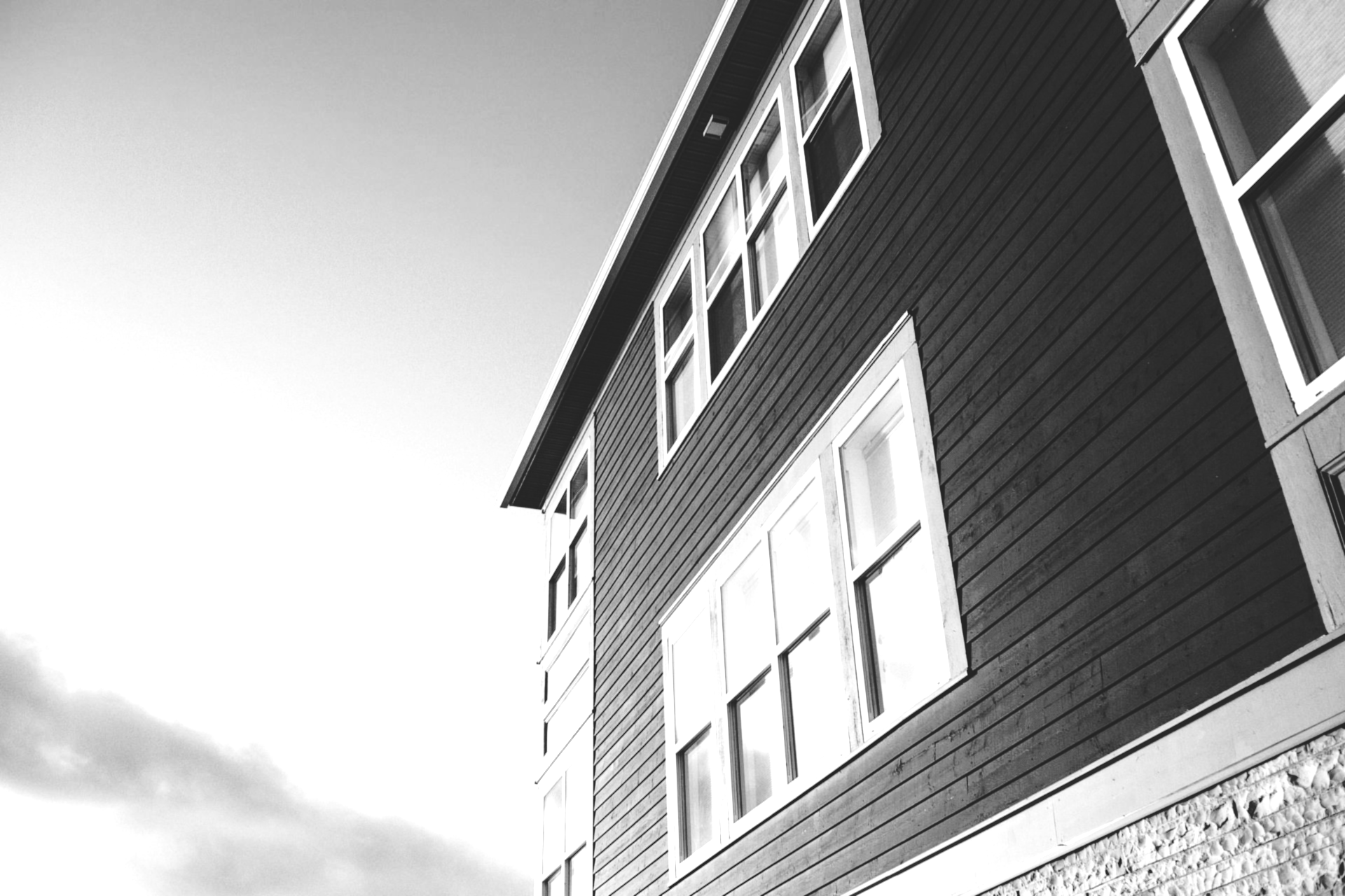Black-and-white view of a tall house with windows against a cloudy sky