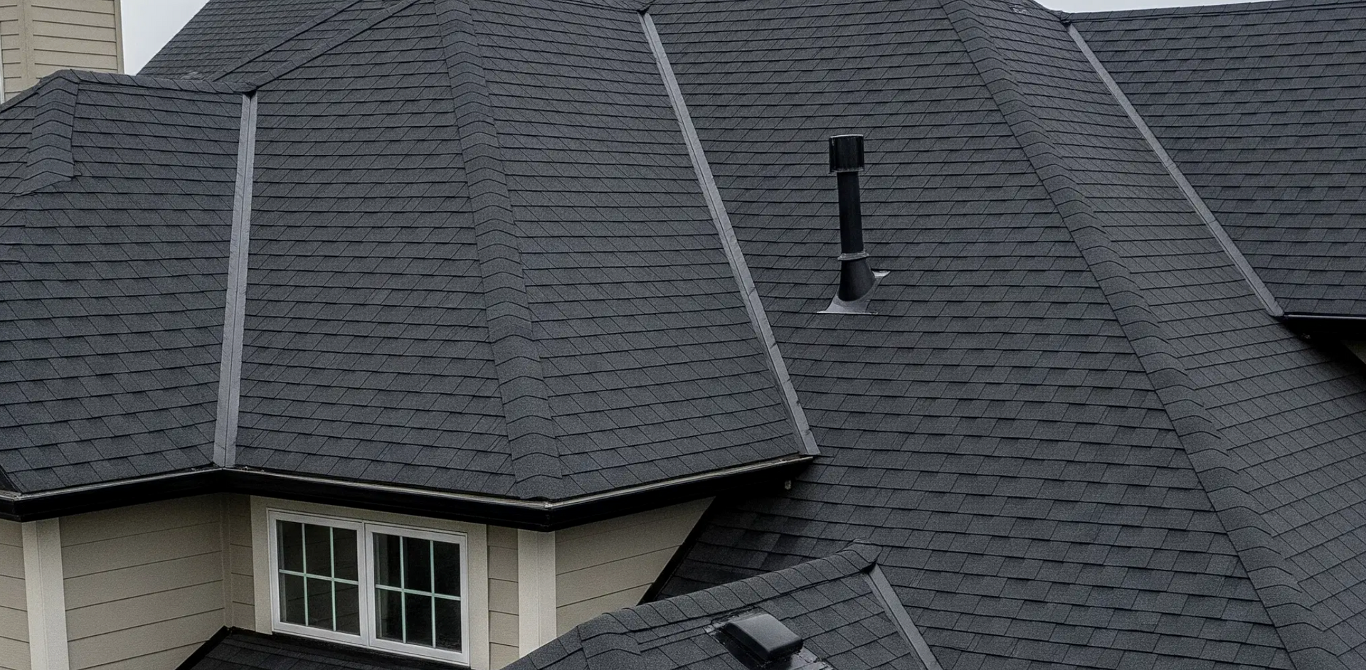 Dark gray shingled house roof with a vent pipe and dormer windows
