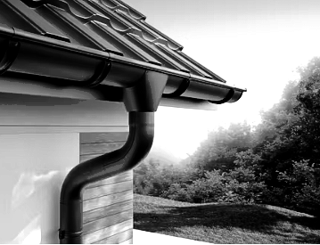 Black rain gutter and downspout on a house roof, with trees and lawn in the background