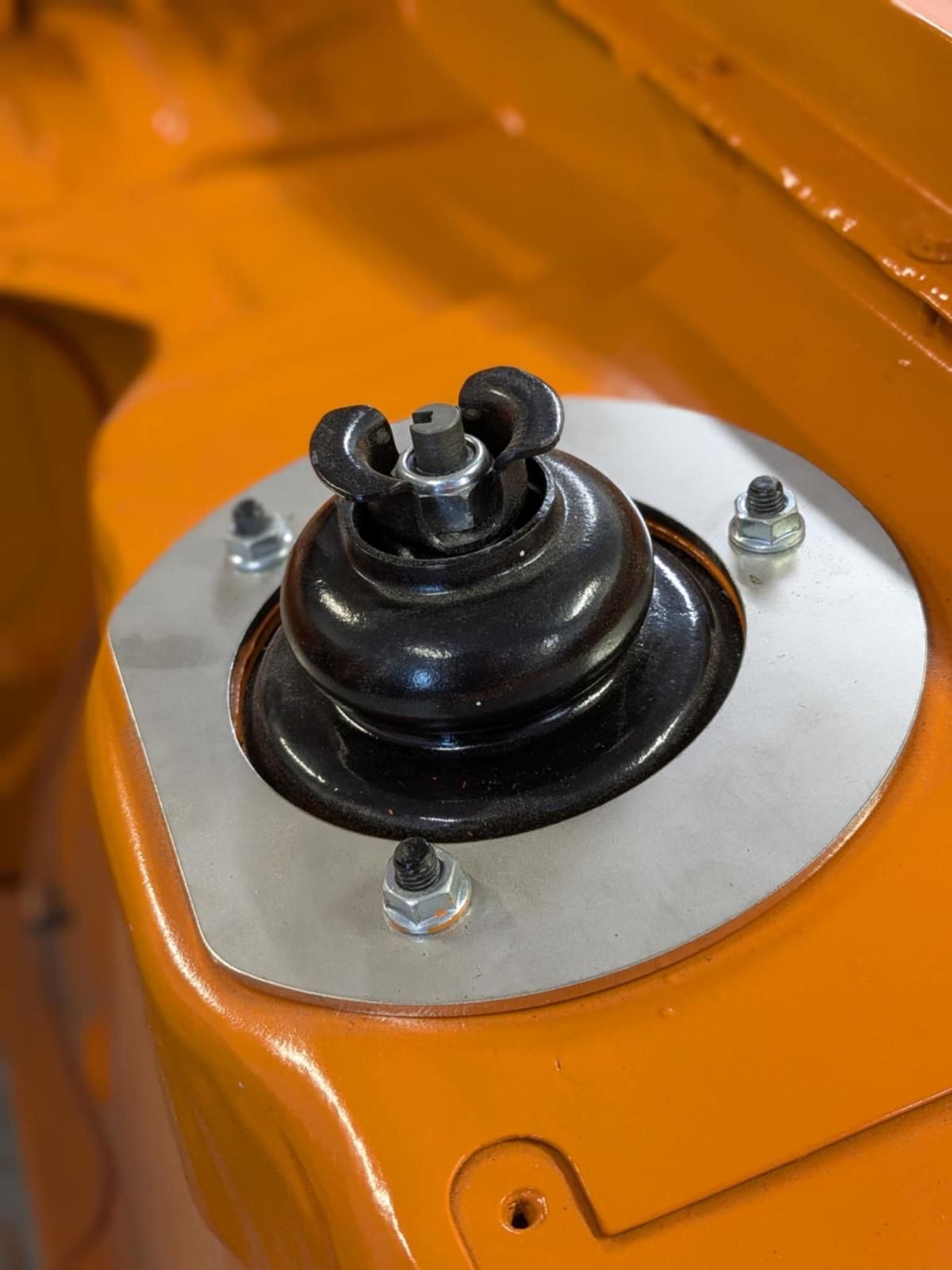 Close-up of a black car suspension top mount on an orange body panel with silver bolts