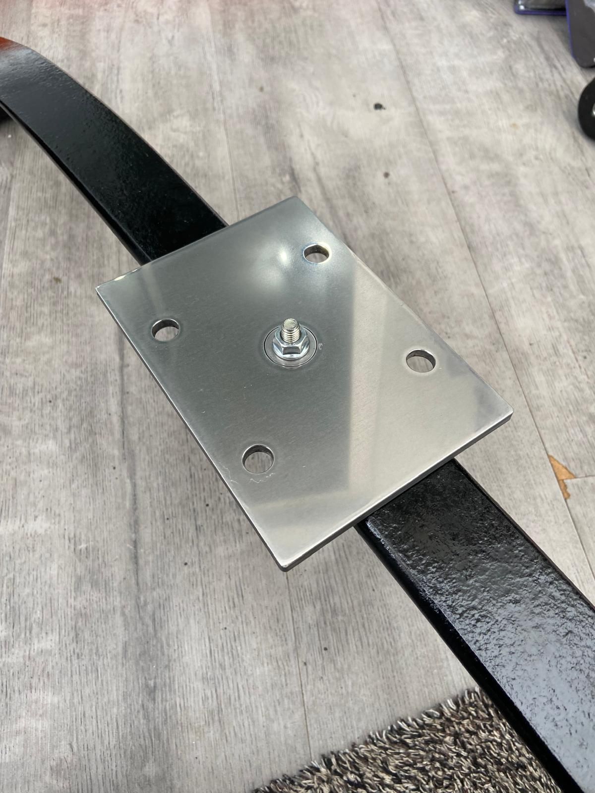Metal mounting plate with four holes bolted to a black curved bar on a gray floor.