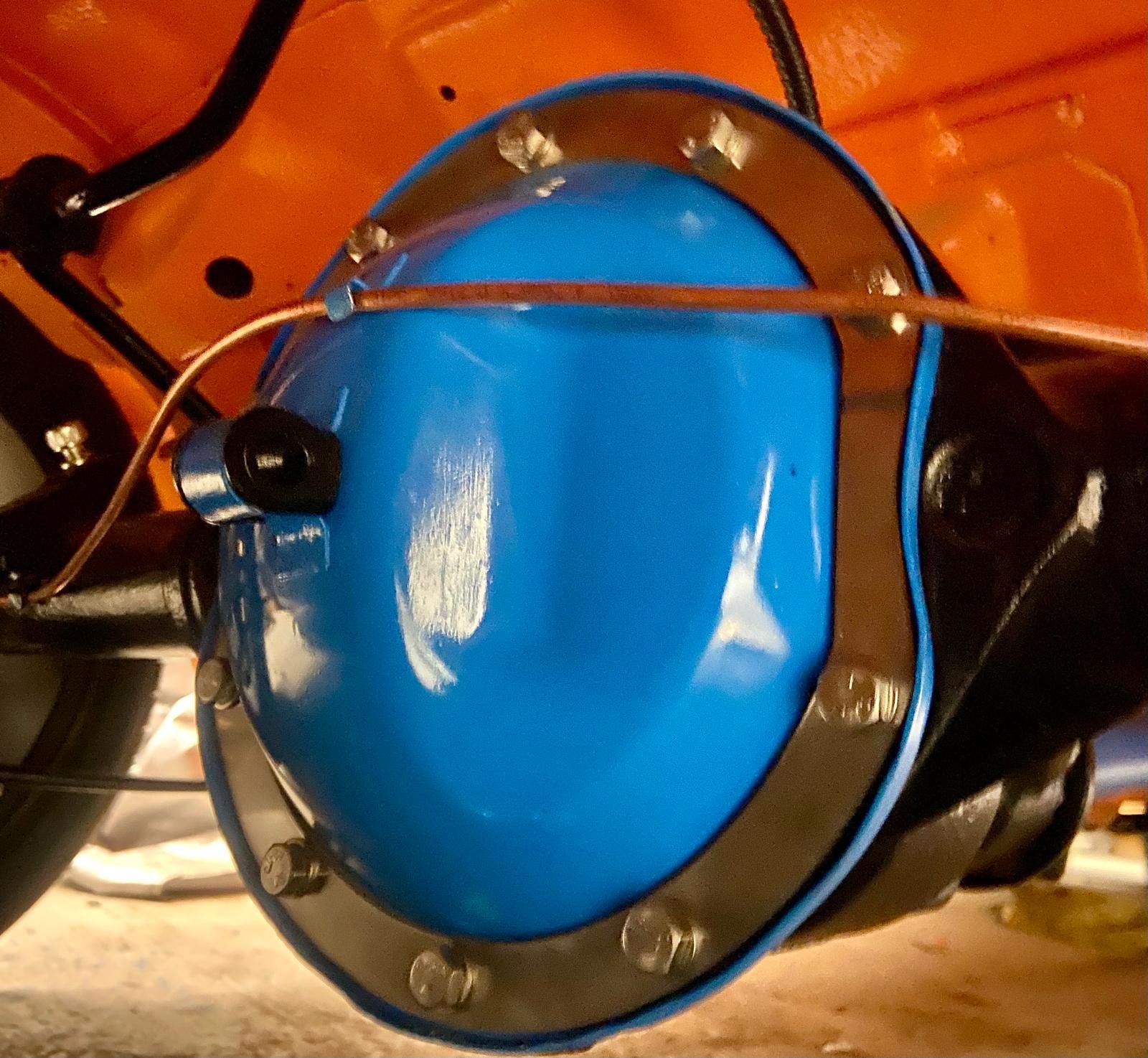 Blue metal gear cover with bolts and copper tubing on an orange machine.