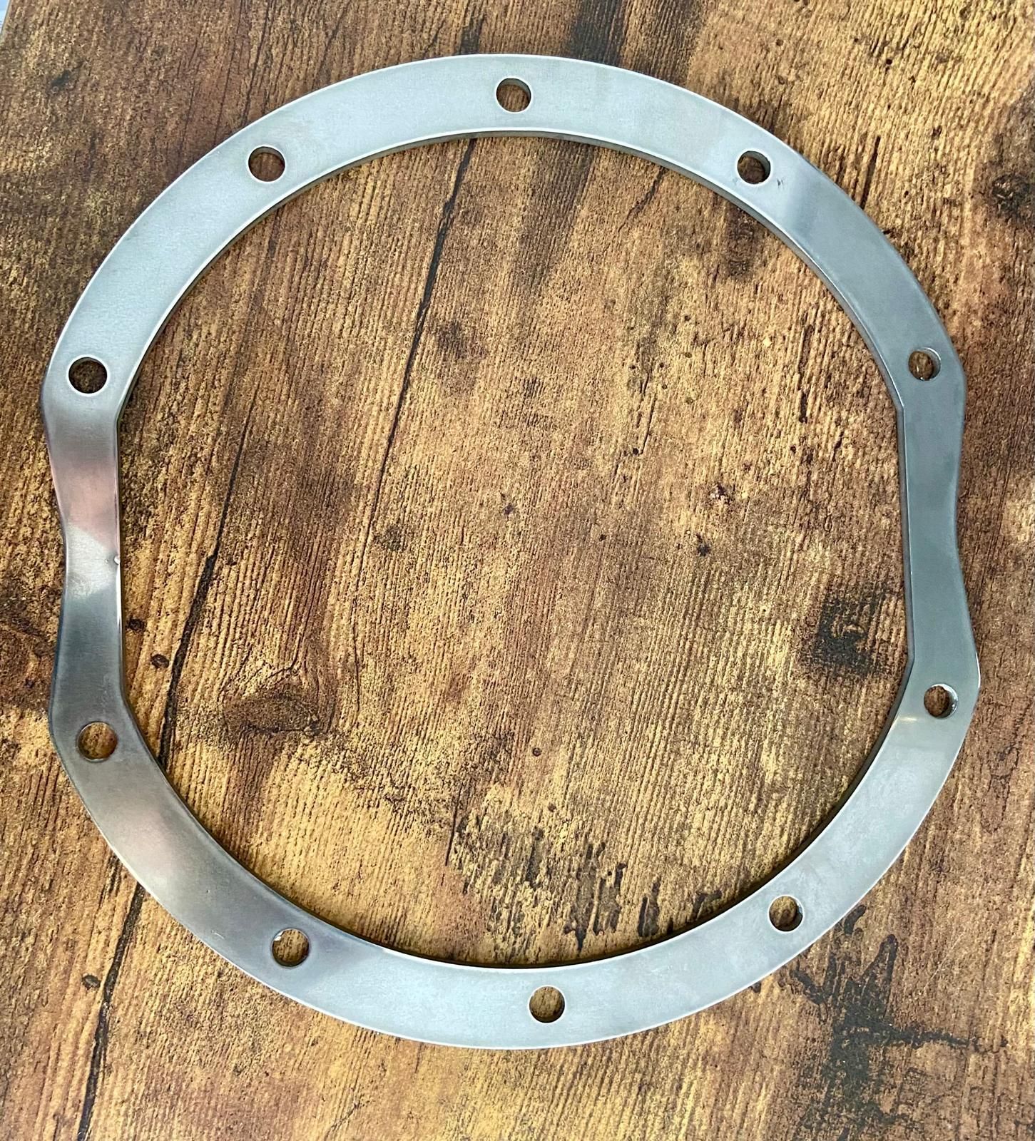 Silver metal gasket ring with bolt holes on a wooden surface