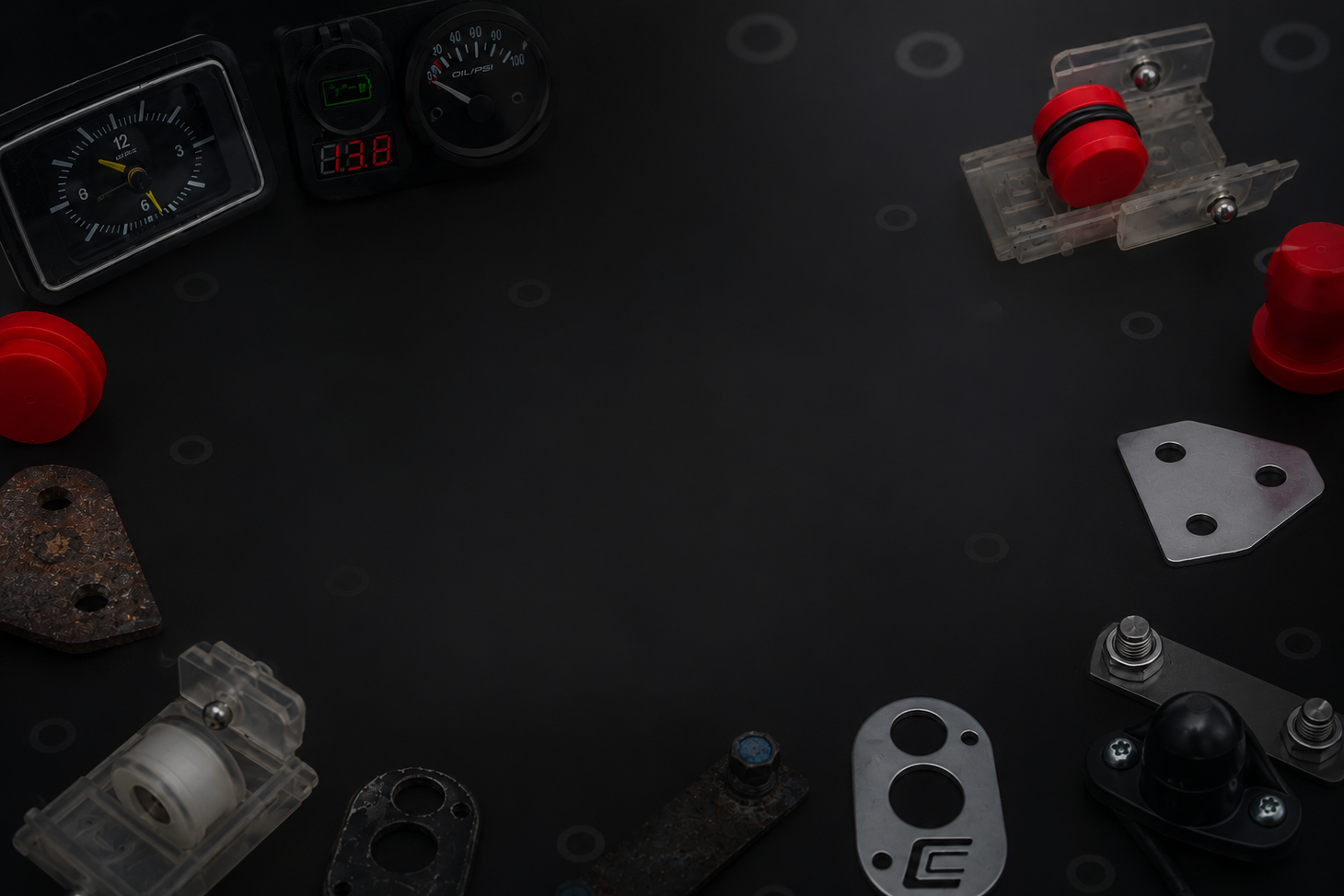Scattered mechanical parts and red components on a dark workbench, with gauges in the background