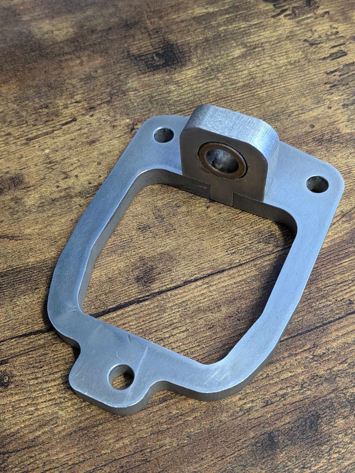 Silver metal gasket plate with bolt holes on a wooden surface