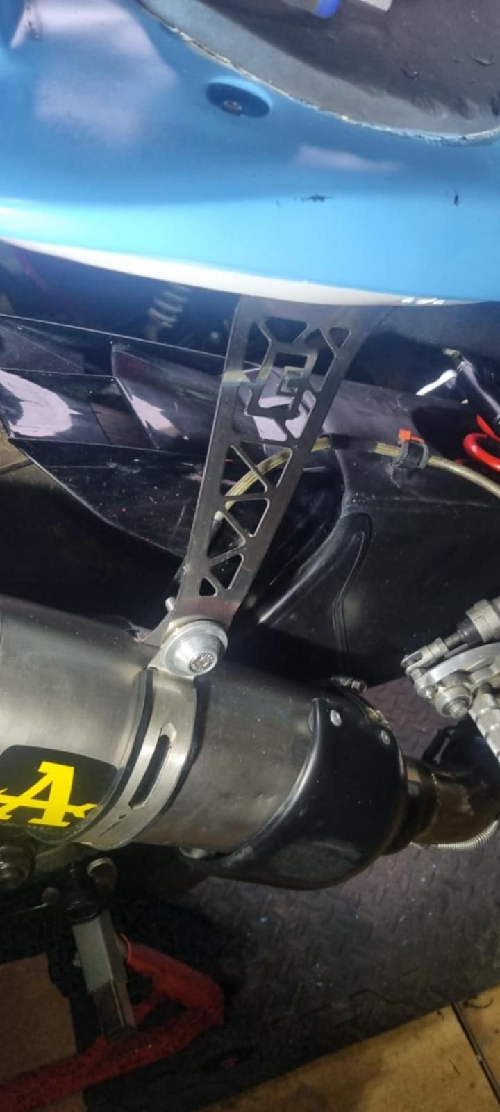 Close-up of a modified car exhaust and rear underbody with blue bodywork and metal support bracket