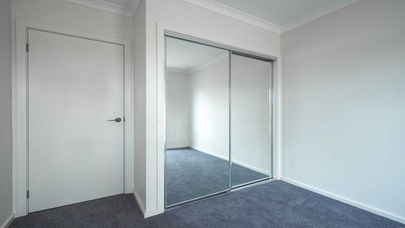 Empty room with white walls, gray carpet, mirrored closet doors, and a closed white door.