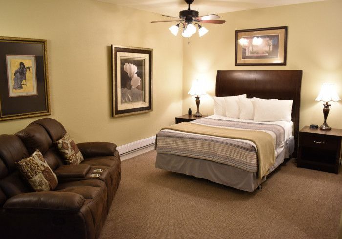Cozy bedroom with a bed, brown leather sofa, framed wall art, nightstands, and a ceiling fan.