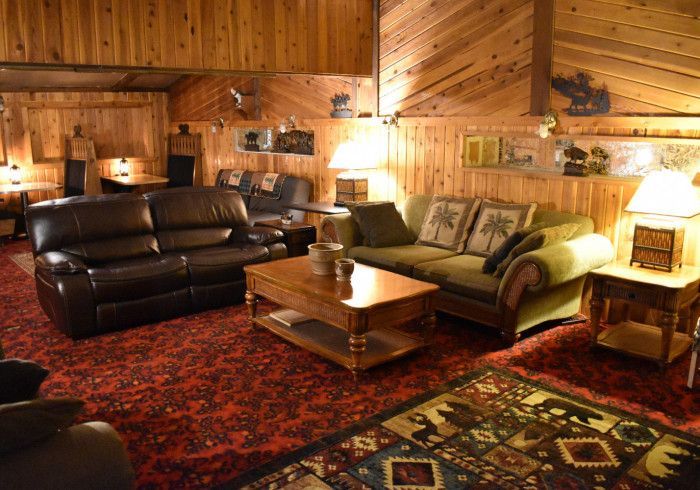 Cozy log cabin living room with leather sofas, coffee table, lamps, and a red patterned rug
