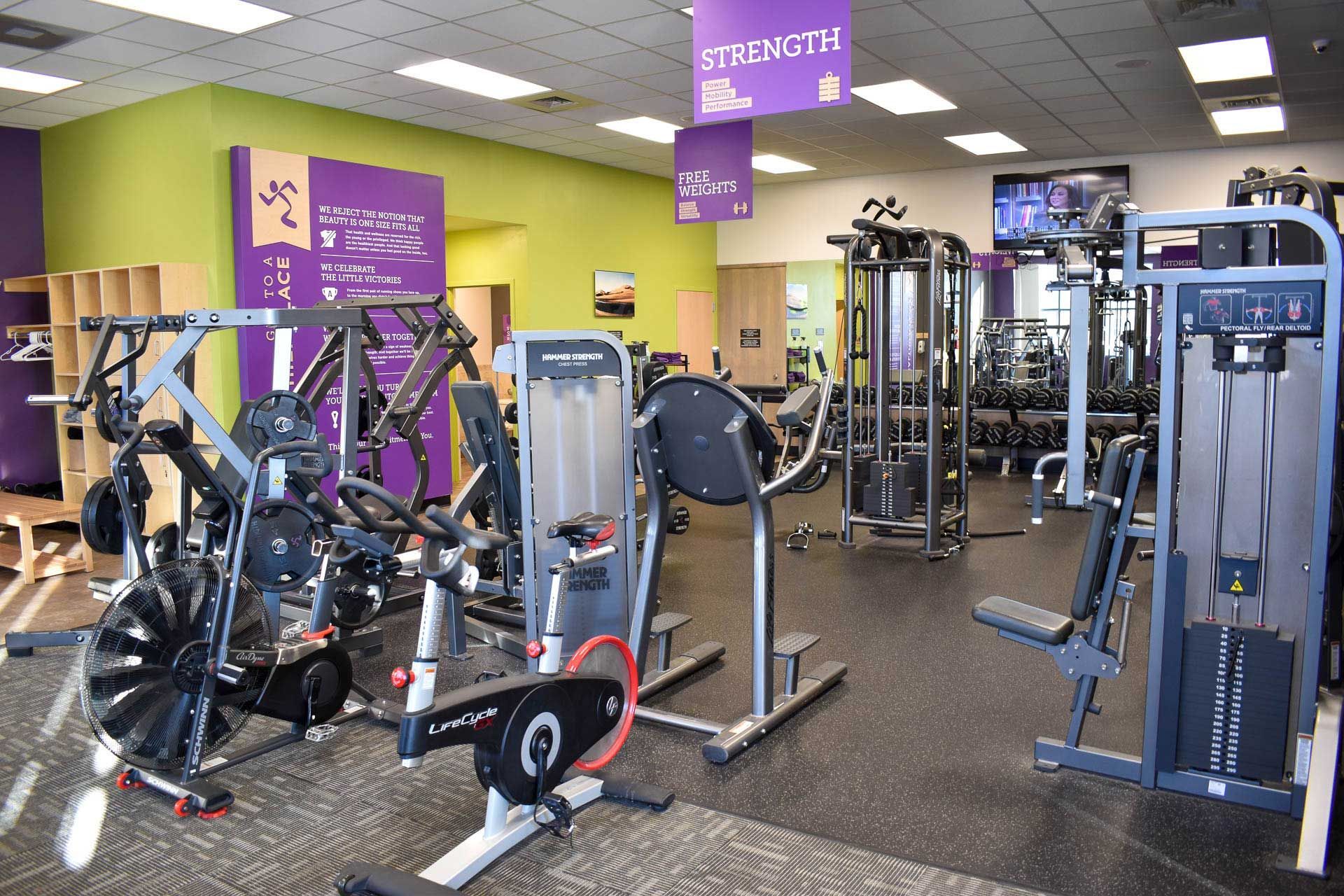 Bright gym interior with weight machines, exercise equipment, and purple wall signs.