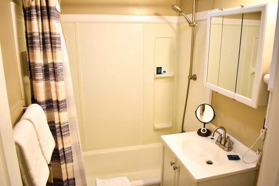 Small beige bathroom with a shower/tub, sink, mirror, and striped shower curtain