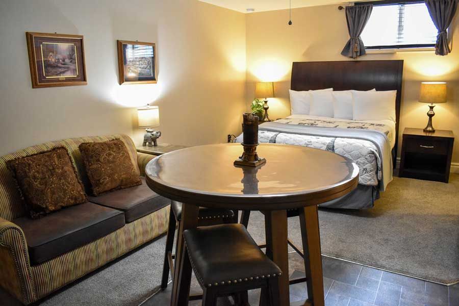 Cozy bedroom sitting area with round table, sofa, bed, lamps, and warm beige decor