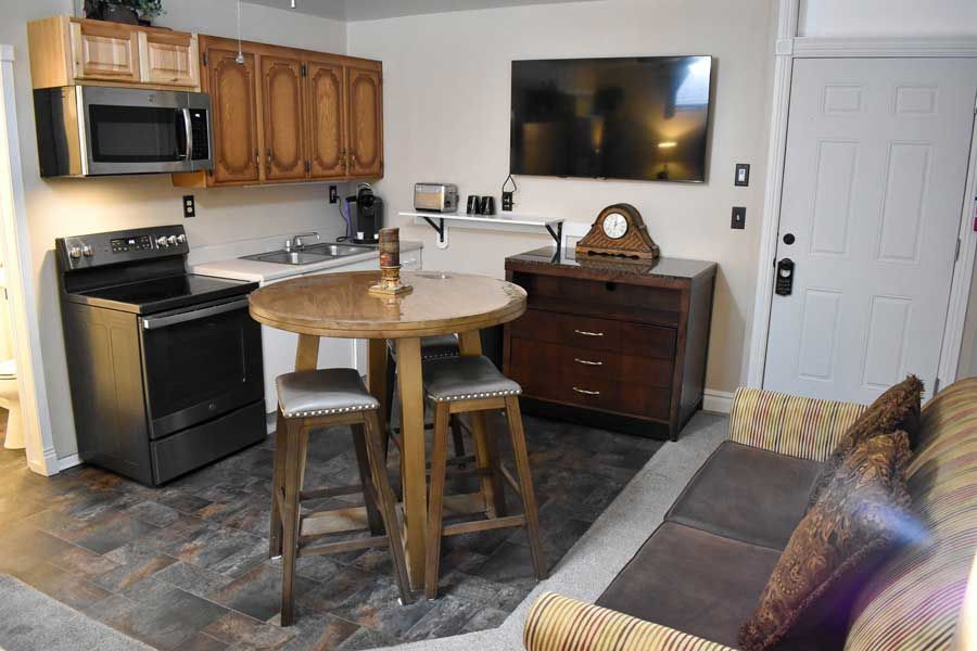 Compact kitchen and dining area with black appliances, round wooden table, wall-mounted TV, and cabinet storage.