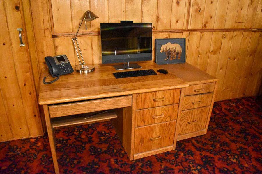 Wood-paneled office with a wooden desk, computer, lamp, phone, and bear picture on the wall.