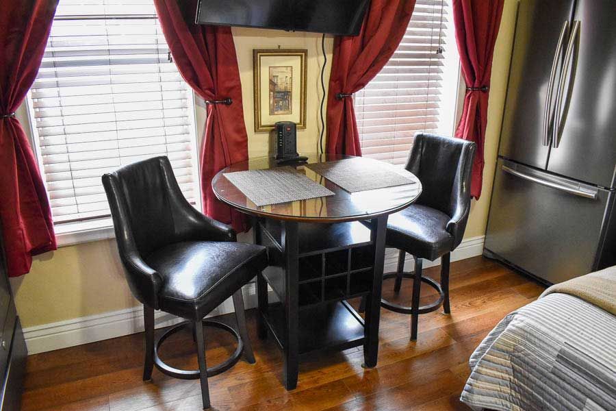 Small dining nook with two black chairs, a round table, and red curtains beside a window.