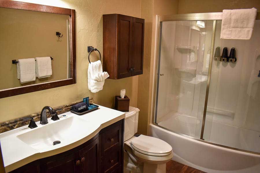 Bathroom with vanity, mirror, toilet, bathtub, and wooden cabinets in warm beige tones