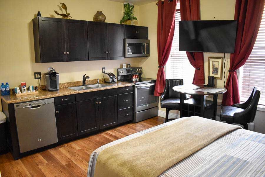 Modern studio room with kitchenette, TV, desk, and bed by red curtains
