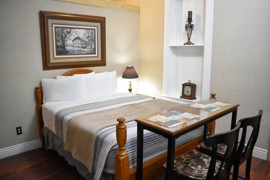 Small bedroom with twin bed, desk, framed art, and built-in shelves with lamp and clock.