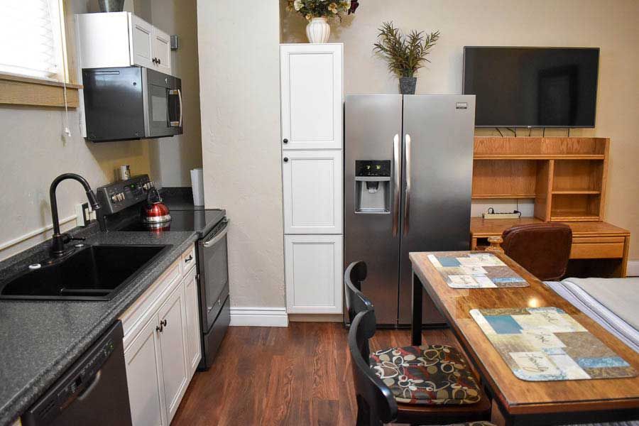 Modern kitchen and dining area with stainless steel fridge, black countertops, and wooden table.