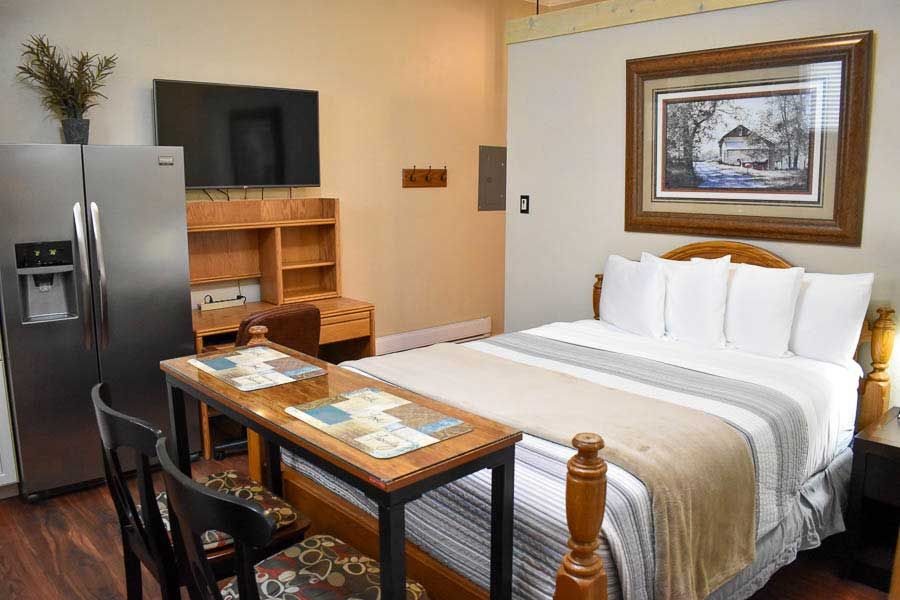 Hotel room with a double bed, desk, TV, mini fridge, and wooden shelving