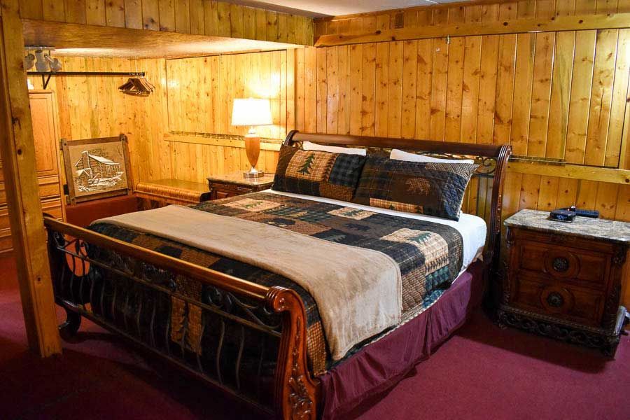 Cozy wooden bedroom with a bed, bedside lamp, and burgundy carpet