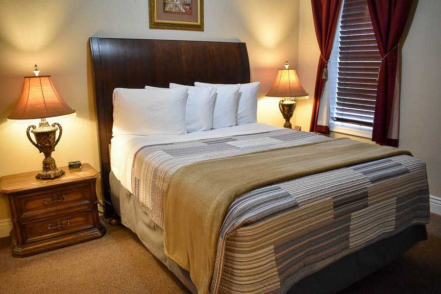 Neatly made bed in a warm hotel room with bedside lamps and burgundy curtains