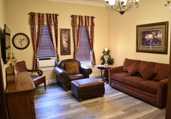 Cozy living room with brown sofa, armchair, ottoman, window blinds, and framed wall art