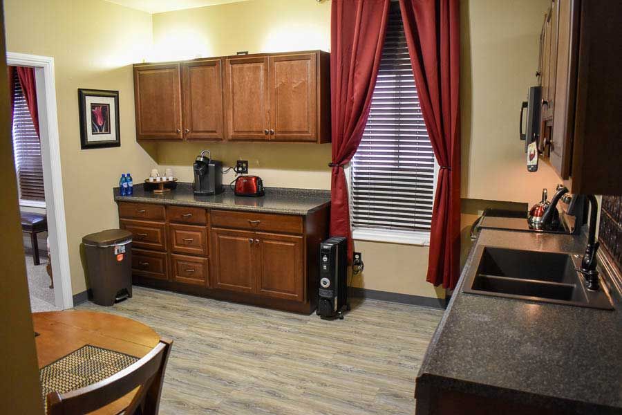 Kitchen with wooden cabinets, black countertops, a sink, and a window with red curtains.
