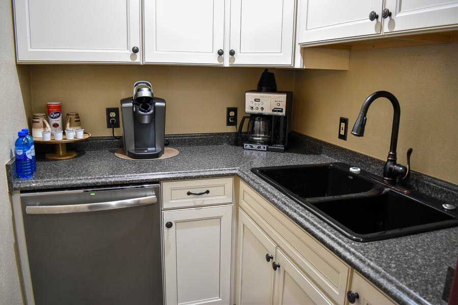Compact kitchen with white cabinets, black granite counters, sink, dishwasher, and coffee maker.