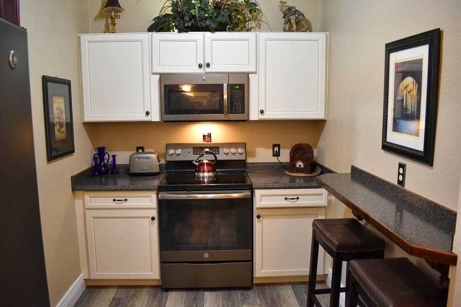 Compact kitchen with white cabinets, black stove, beige counters, and a small dining nook on the right.