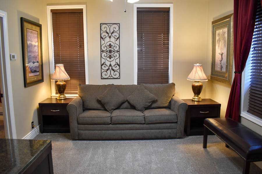 Living room with gray sofa, two lamps, two windows, and wall art