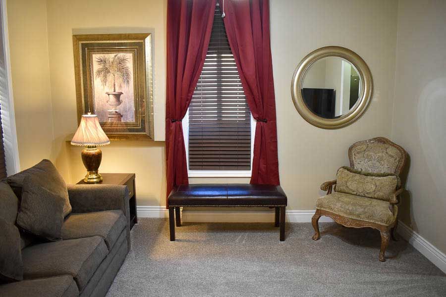 Cozy living room with gray sofa, lamp, red curtains, round mirror, and floral chair