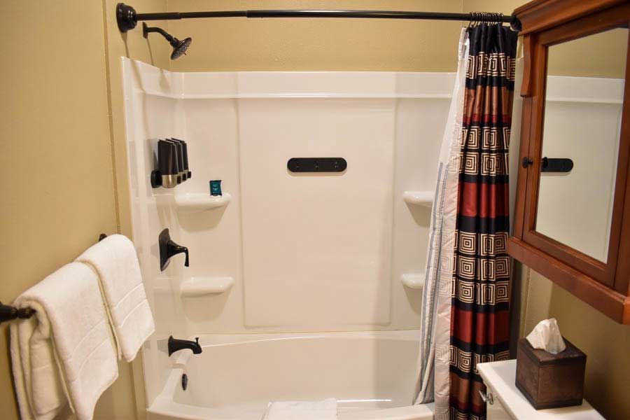 Accessible bathroom with grab bars, shower bench, tub, towels, and a plaid shower curtain