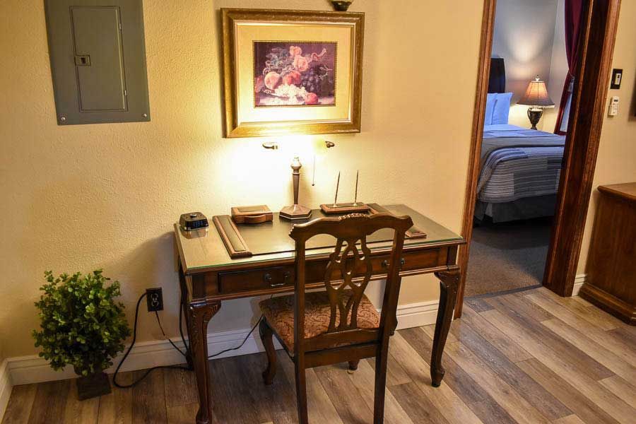 Small dining nook with a wooden table, two chairs, lamp, plant, and a bedroom visible through the doorway.