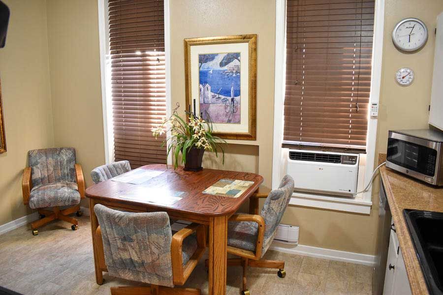 Small dining area with wooden table, four chairs, wall art, and windows with blinds and a window AC unit.