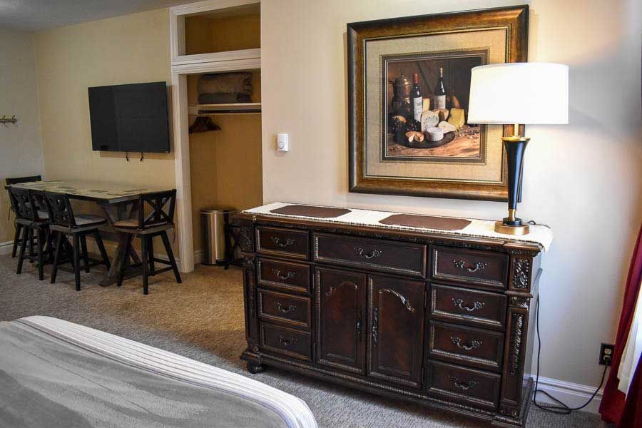 Hotel room with dark wood dresser, wall-mounted TV, desk, chair, and bed edge in view.