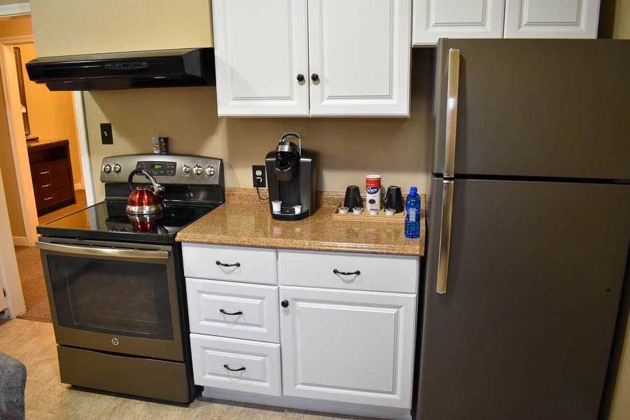 Small kitchen with stove, countertop, cabinets, coffee maker, and stainless steel refrigerator.