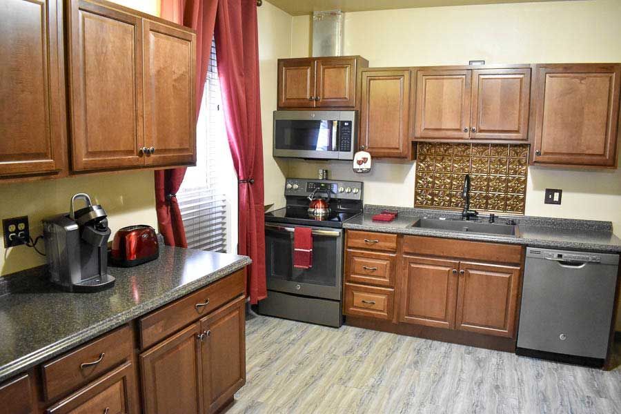 Compact kitchen with wooden cabinets, granite counters, red curtains, and stainless appliances.