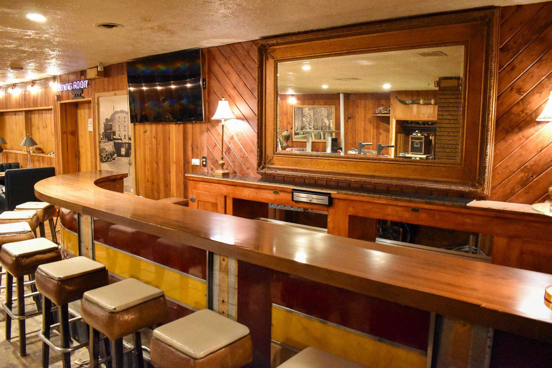 Wood-paneled bar with a long wooden counter, stools, and a large mirror behind it
